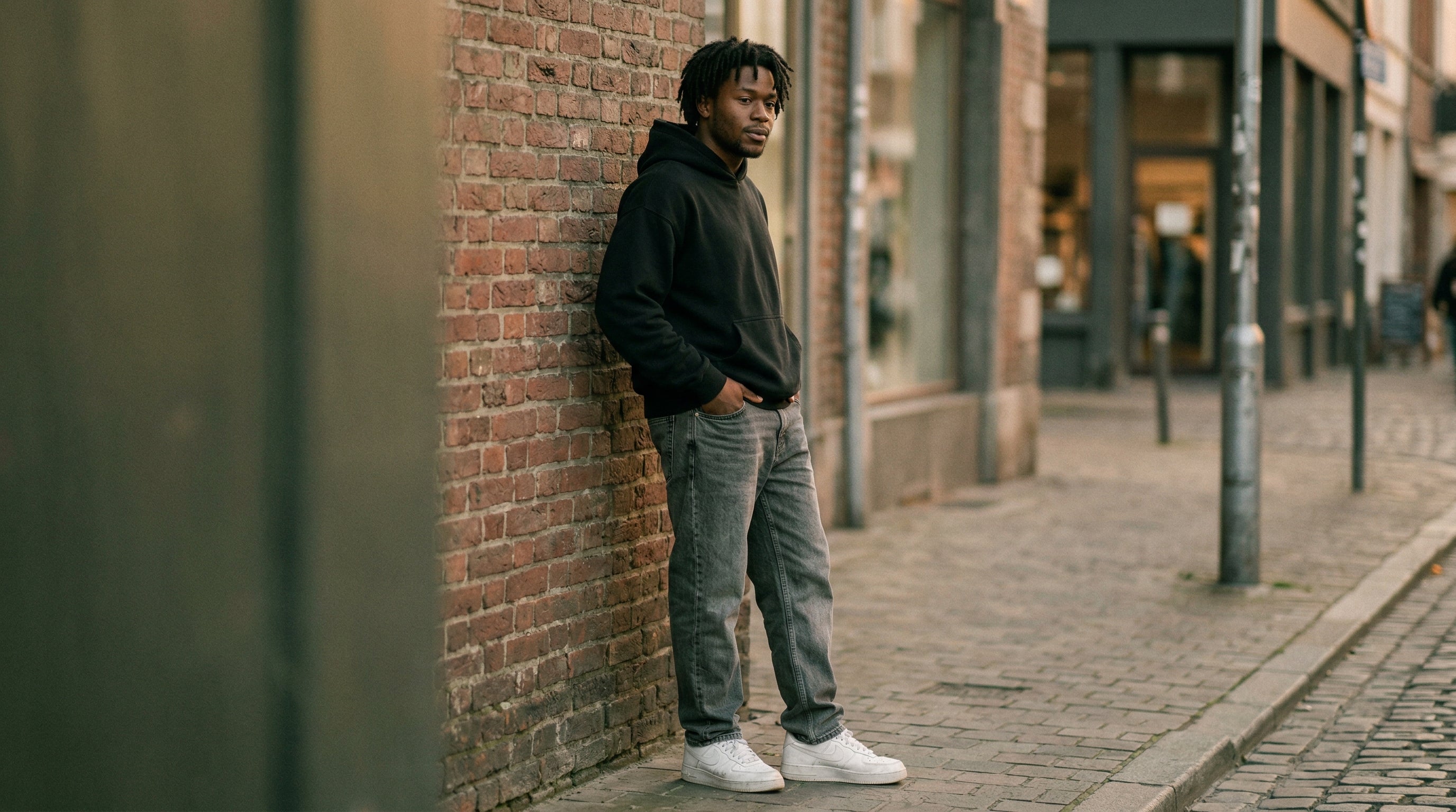 Oversized schwarzer Hoodie und baggy graue Jeans an Backsteinmauer auf urbanem Gehweg