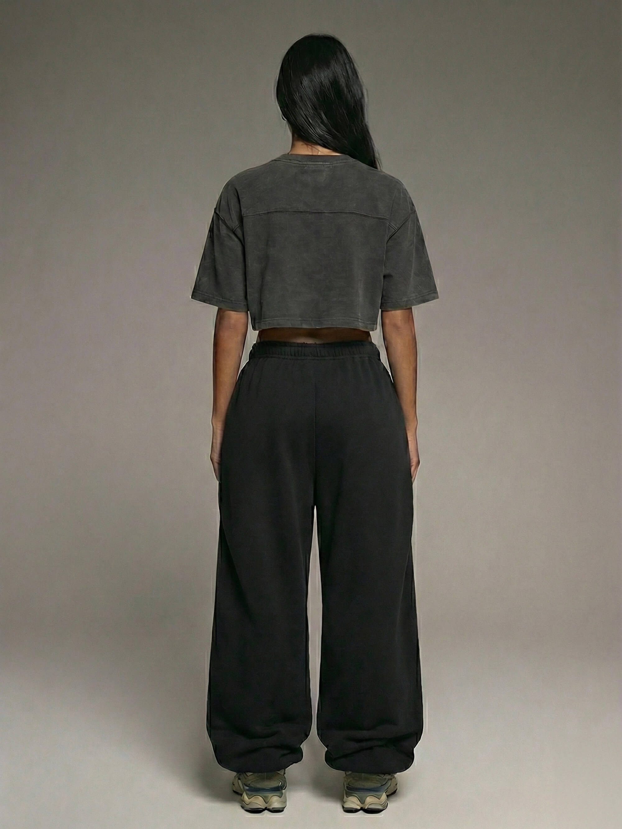 Baggy Jogger Sweatpants in Black an einer Frau, Rückansicht im Studio, weiter Relaxed Fit mit elastischem Bund und fallendem Bein