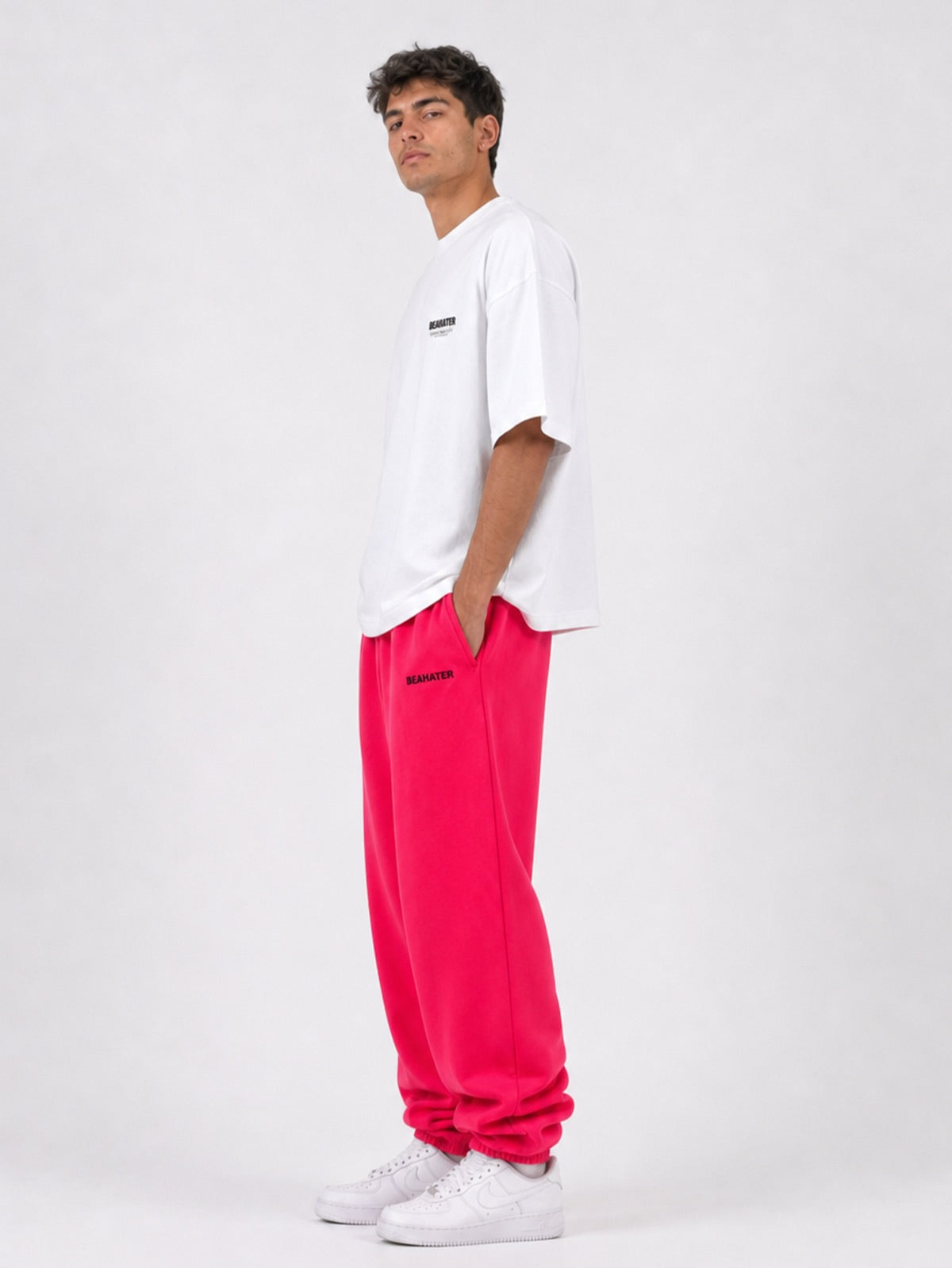 Pinke Baggy Jogger Seitenansicht am Herren-Model, Hände in den Taschen mit weißem Oversize Tee