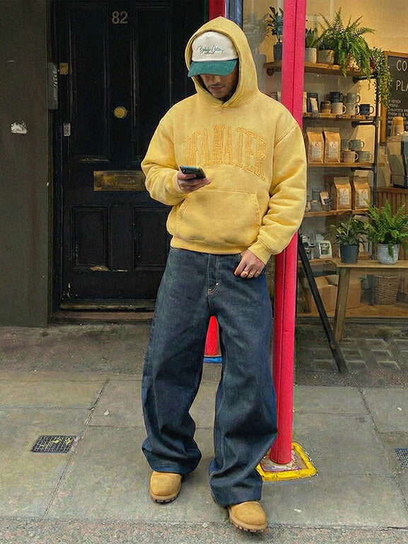Model trägt Beahater Oversized Hoodie in Mustard Yellow im urbanen Street Look vor Café