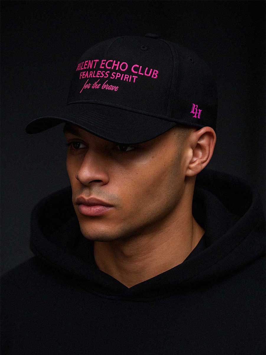 Schwarze Baseball Cap mit pinker „RELENT ECHO CLUB – FEARLESS SPIRIT – for the brave“ Stickerei, getragen von Model in schwarzem Hoodie – Streetwear Look für mutige Charaktere.