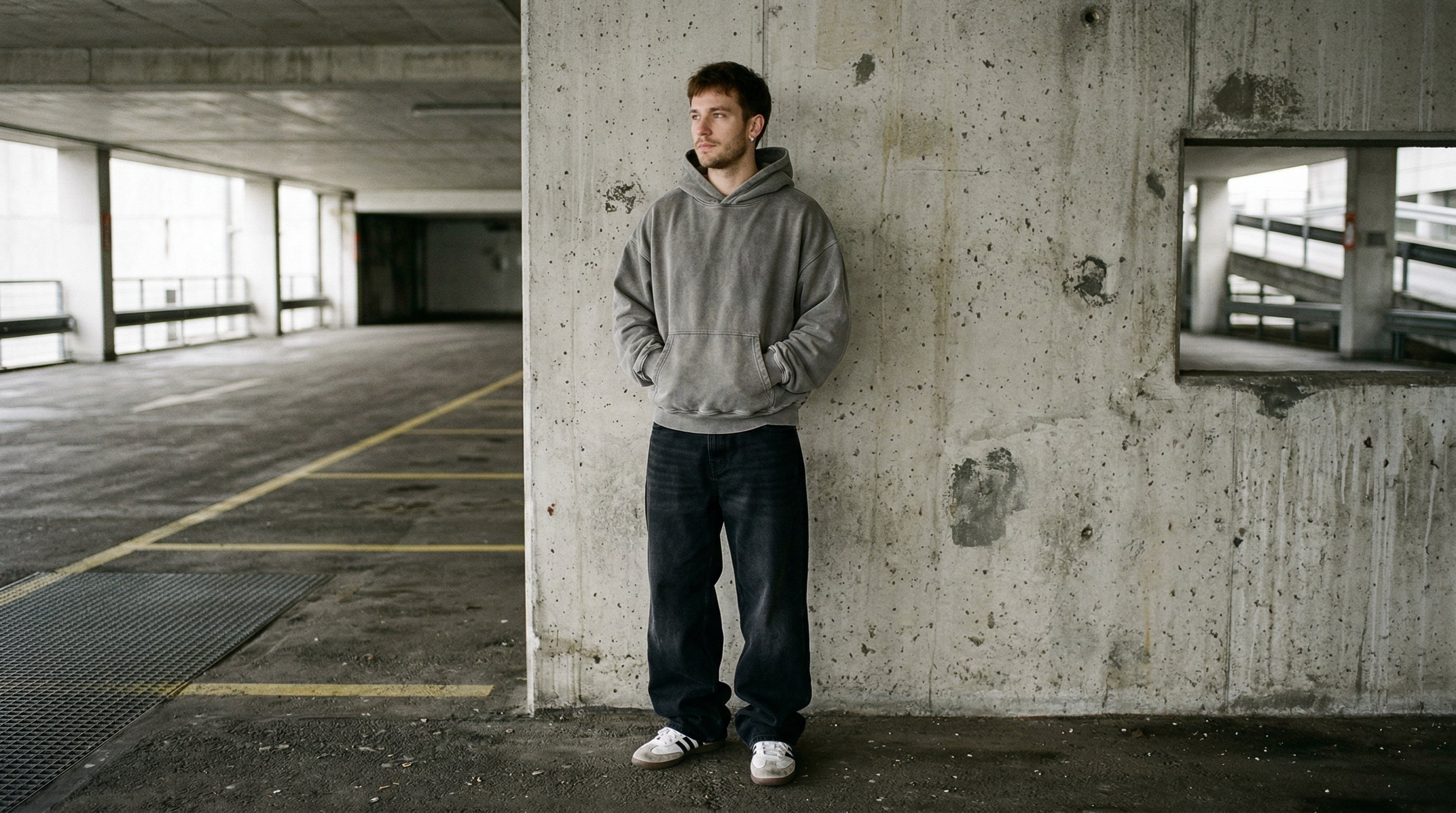 Mann in grauem Oversize Hoodie und Baggy Jeans an Betonwand, urbaner Streetwear Look