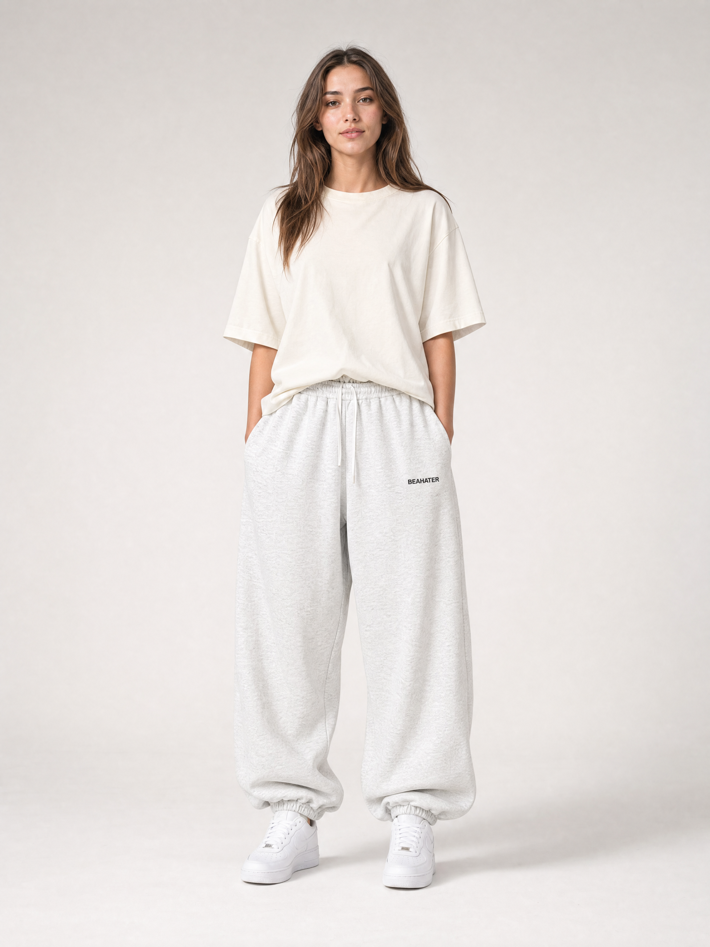 Jogger baggy off grey në model femër, pamje ballore, prerje oversized e lirshme, atlete të bardha