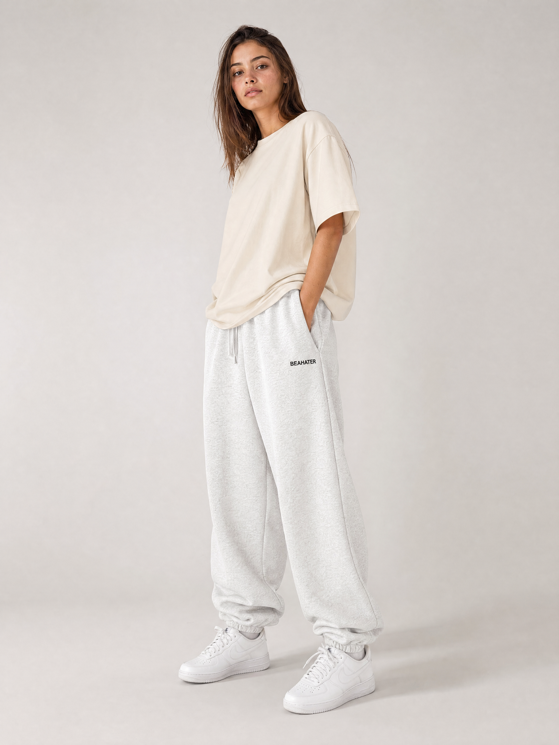 Jogger baggy off grey në model femër, pamje anësore, prerje e gjerë, atlete të bardha