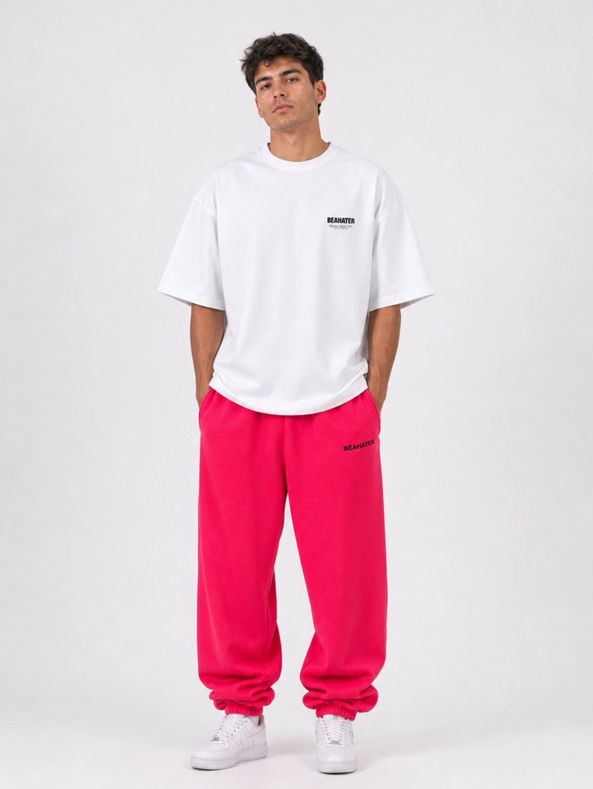 Pinke Baggy Jogger Herren am Model in Frontansicht, Hände in den Taschen mit weißem Oversize Tee