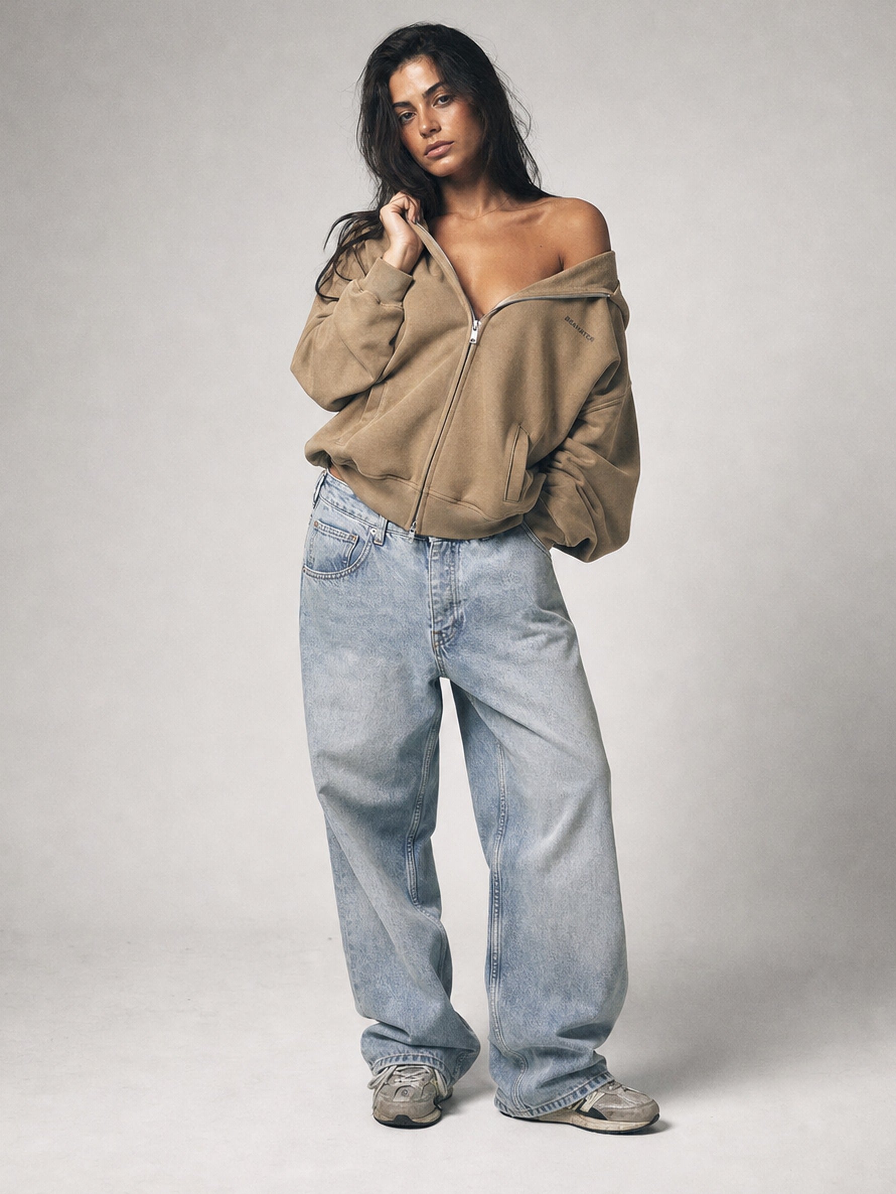 Weibliches Model trägt Mocha Mousse Zip Hoodie lässig über der Schulter, Oversized Fit kombiniert mit Baggy Jeans